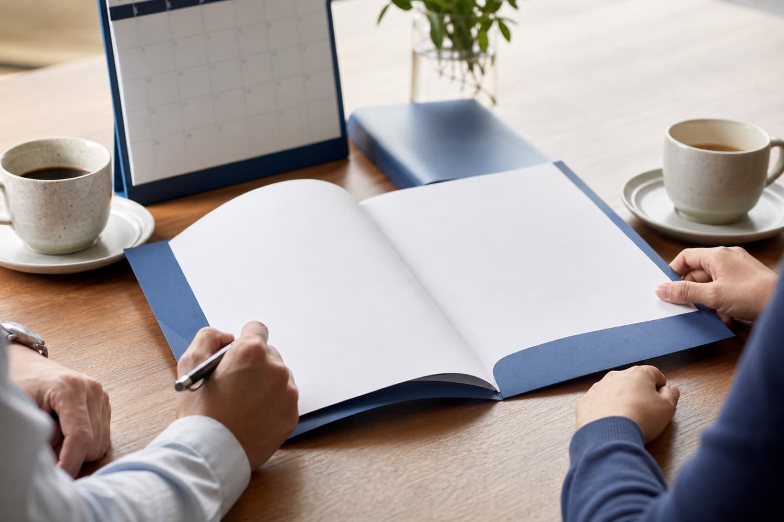 Two people reviewing a blank agreement beside a calendar and coffee
